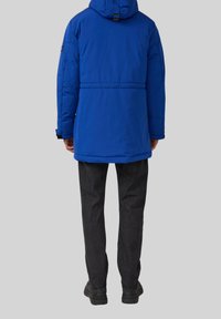 Blaues Pufferjacke mit Kapuze, elastischen Bündchen und verstellbarem Bund. Tragen mit dunkelgrauen Hosen und schwarzen Schuhen. Rückenansicht.