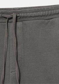 Gros plan de la ceinture en tissu gris d’un pantalon de survêtement avec un cordon noué en boucle et une couture visible de la poche latérale.