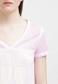 Ljusrosa V-ringad t-shirt med nätstruktur och korta ärmar. Har ett lätttryck på framsidan och en avslappnad passform.