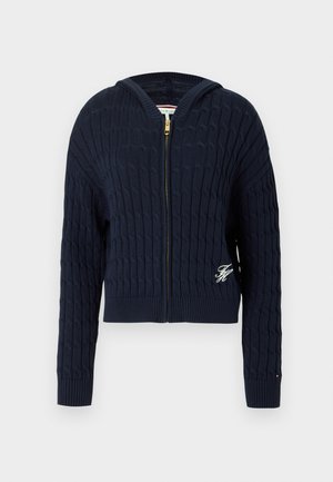 Marineblå strikket sweater med lynlås, kabelmønster, ribbet nederste kant og manchetter, med et lille broderet logo på forsiden.