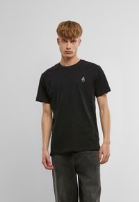 Svart bomulls t-skjorte med rund hals. Har en liten hvit grafisk logo på venstre bryst. Casual passform, enkel design med korte ermer.