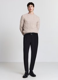 Maglione beige a trecce, pantaloni neri su misura con passanti per cintura e fibbia circolare argentata, abbinati a stivaletti neri in pelle.