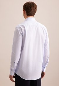 Camicia a maniche lunghe azzurro chiaro con una trama sottile, colletto con bottoni e silhouette aderente. Presenta accenti a contrasto sui bottoni dei polsini.