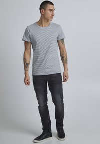 Harmaa raidallinen t-paita pyöreällä pääntiellä yhdistettynä slim fit mustiin farkkuihin ja mustiin lenkkareihin. Yksinkertainen muotoilu, puuvillamainen rakenne.