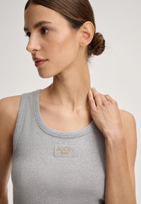 Grijs geribbeld tanktop met een ronde hals. Heeft een geweven label met de tekst "JOOP! JEANS" in het goud. Toont het profiel van het model met haar in een chignon.