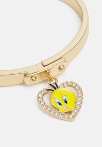 Zelta tonī izgatavota bangles aproce ar sirsniņas piekariņu, kas satur dzeltenu simbolu un caurspīdīgu rhinestone akcentus, gluda metāla apdare.