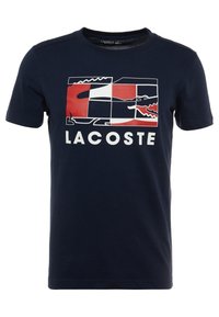Námořnické bavlněné tričko s grafickým potiskem v červené, bílé a černé barvě s logem Lacoste a designem krokodýla. Krátké rukávy a kulatý výstřih.