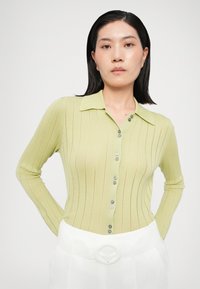 Light green ribbed knit cardigan with a collared neckline, featuring button closure and subtle vertical stripes, paired with white high-waisted pants.