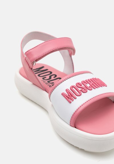 Rosa och vit sandal med en bred rem som har "MOSCHINO" i rosa broderi. Tjock vit sula, vadderad ankelsnodd och slät yta.