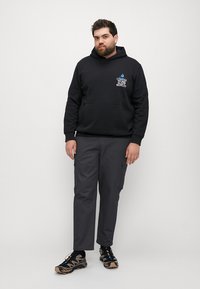 Schwarzer Kapuzenpullover mit Fronttasche und weißem Grafiktext. Graue Cargohose mit Seitentaschen. Schwarz-graue Sneaker mit strukturiierter Sohle.