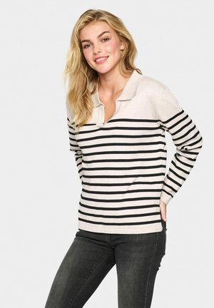 Light beige long-sleeve polo with black horizontal stripes, featuring a V-neckline and ribbed cuffs, worn with dark jeans.