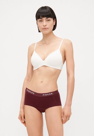 Reggiseno bianco con spalline sottili e design liscio e sagomato; abbinato a mutandine maroon con una cintura bianca "PIECES".