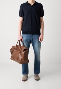 Polo à manches courtes bleu marine, jean bleu, sac de voyage en cuir marron clair avec fermetures éclair, et baskets grises. Textures lisses et coupe ajustée.