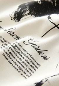 Cotton fabric featuring black printed text on a white background, with visible texture and undulating folds, displaying intricate patterns and details.