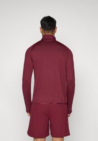 Burgundi pikkade varrukatega särk kõrge kaelusega, valmistatud siledast kangast. Sellel on raglaani varrukad ja sirge äär, ning see sobib kokku vastavate lühikeste pükstega.