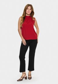 Blusa rossa senza maniche con scollo arricciato, abbinata a pantaloni neri a vita alta e scarpe con tacco a blocco con stampa leopardata.