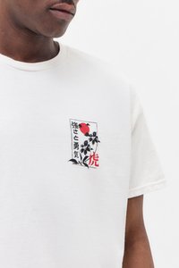 Kortermet hvit T-skjorte med et fargerikt brodert lapp med røde, svarte og blå design og japansk tekst på brystet.
