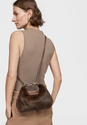Woman wearing sleeveless beige top and pants, carrying a small brown furry handbag with a leather strap over her shoulder.