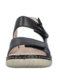 Sandales en cuir noir avec des brides croisées et une boucle, dotées d'une semelle texturée de couleur claire et de détails de couture visibles.