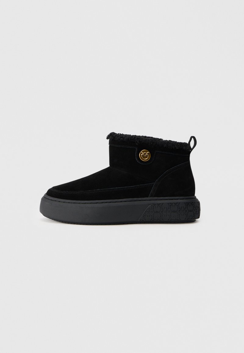 Botas de tornozelo pretas com parte superior em camurça, acabamento em pelo luxuoso, um emblema dourado redondo e uma sola de borracha grossa e texturizada.