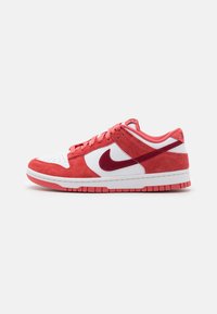 Nízkopriemerné tenisky s bielym koženým základom, červenými semišovými prekrytiami, červeným Nike swooshom a červenou gumovou podrážkou na bielom pozadí.