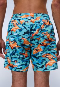 Bañador con un patrón vibrante de naranja, azul y negro. Presenta una cinturilla elástica y un bolsillo trasero. Está hecho de un tejido ligero.