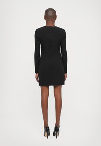 Zwart langemouwen jurk met een getailleerde silhoette, rits aan de achterkant en een zoom boven de knie. Gemaakt van glad, rekbaar materiaal.