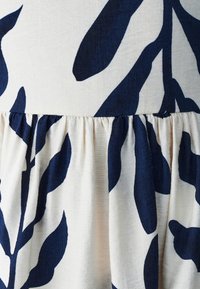 Nærbillede af sammenfoldet stof med navyblåt bladmønster på cremefarvet baggrund, der viser tekstur og sømdetaljer.