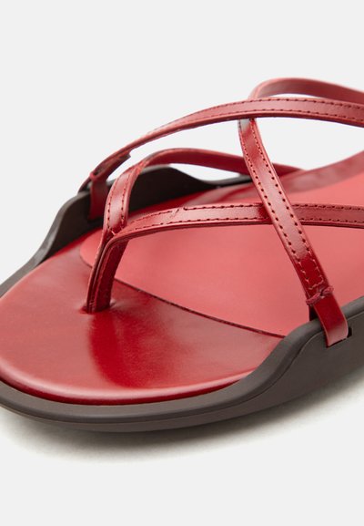 Κόκκινο δερμάτινο σανδάλι με λεπτά σταυρωτά λουριά και καφέ σόλα, εμφανιζόμενο σε κοντινή λοξή γωνία σε λευκό φόντο.