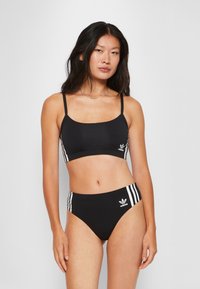 Svart sportbikini-set med en cropped topp med tunna band och en högmidjad botten, båda med vita adidas-ränder och logotypdetaljer.