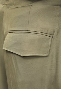 Κοντινό πλάνο σε μπεζ παντελόνι από ύφασμα με τσέπη με καπάκι, εμφανή ραφή και διαγώνια υφή.