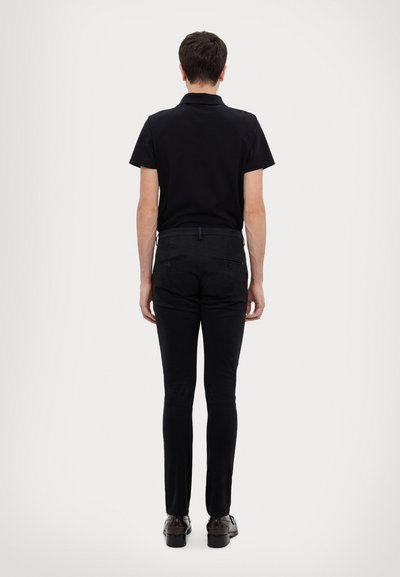 Polo noir à manches courtes, associé à un pantalon noir slim-fit. La tenue présente un design minimaliste et des poches arrière discrètes.
