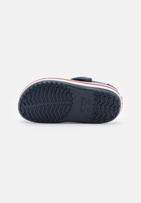 Crocs blu navy con suola in gomma testurizzata, presentano una banda di accento bianca e rossa lungo il bordo. Design resistente e leggero per il massimo comfort.