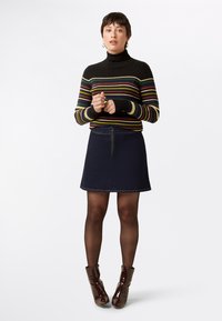 Black turtleneck sweater with multicolored horizontal stripes, paired with a dark denim A-line skirt featuring a front zipper and a circular accent.
