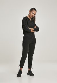 Sudadera negra de manga larga, con cuello redondo y puños acanalados. Combinada con pantalones jogger negros que tienen bolsillos laterales y puños elásticos.