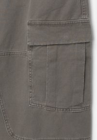 Cargo-pantalon sectie in grijze stof met diagonale weving. Heeft een zijzak met klep en versterkte stiknaden voor duurzaamheid.