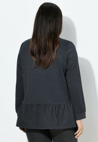 Maglia grigia scura a maniche lunghe con orlo peplum. Realizzata in materiale morbido con una texture liscia e maniche aderenti.