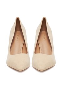 Zapatos de tacón alto de ante beige con punta puntiaguda y empeine bajo, vistos desde arriba sobre un fondo blanco.