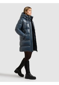 Mörkblå vadderad jacka i glansigt material. Har huva, dragkedja framtill och sidofickor. Matchas med knähöga svarta stövlar.