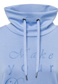 Maglione azzurro chiaro con colletto alto, con coulisse con punte in argento e scritta in rilievo che recita "Fai il tuo." Tessuto dalla texture liscia.