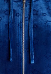 Blauer Kapuzenpullover mit Reißverschluss, gefertigt aus weichem Samtstoff. Verfügt über ein Sternenmuster, zwei Kordelzüge und einen silbernen Reißverschluss auf der Vorderseite.