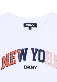 T-shirt en coton blanc avec "NEW YORK" en texte bleu marine et orange, avec un logo DKNY en noir en dessous du texte. Encolure classique.