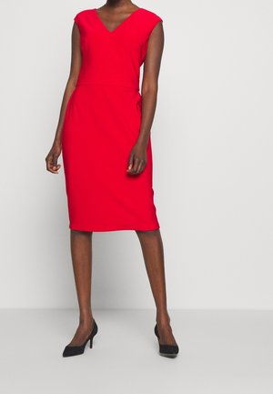 Rode mouwloze jurk met V-hals, getailleerde pasvorm, tot op de knie en een gladde textuur; gecombineerd met zwarte pumps.