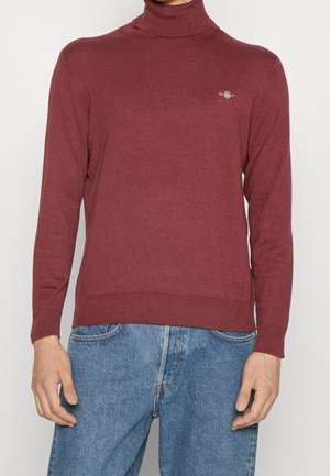 Pull à col roulé bordeaux en tissu tricot doux. Il présente des manches longues, des poignets et un ourlet côtelés, avec un logo subtil sur la poitrine.