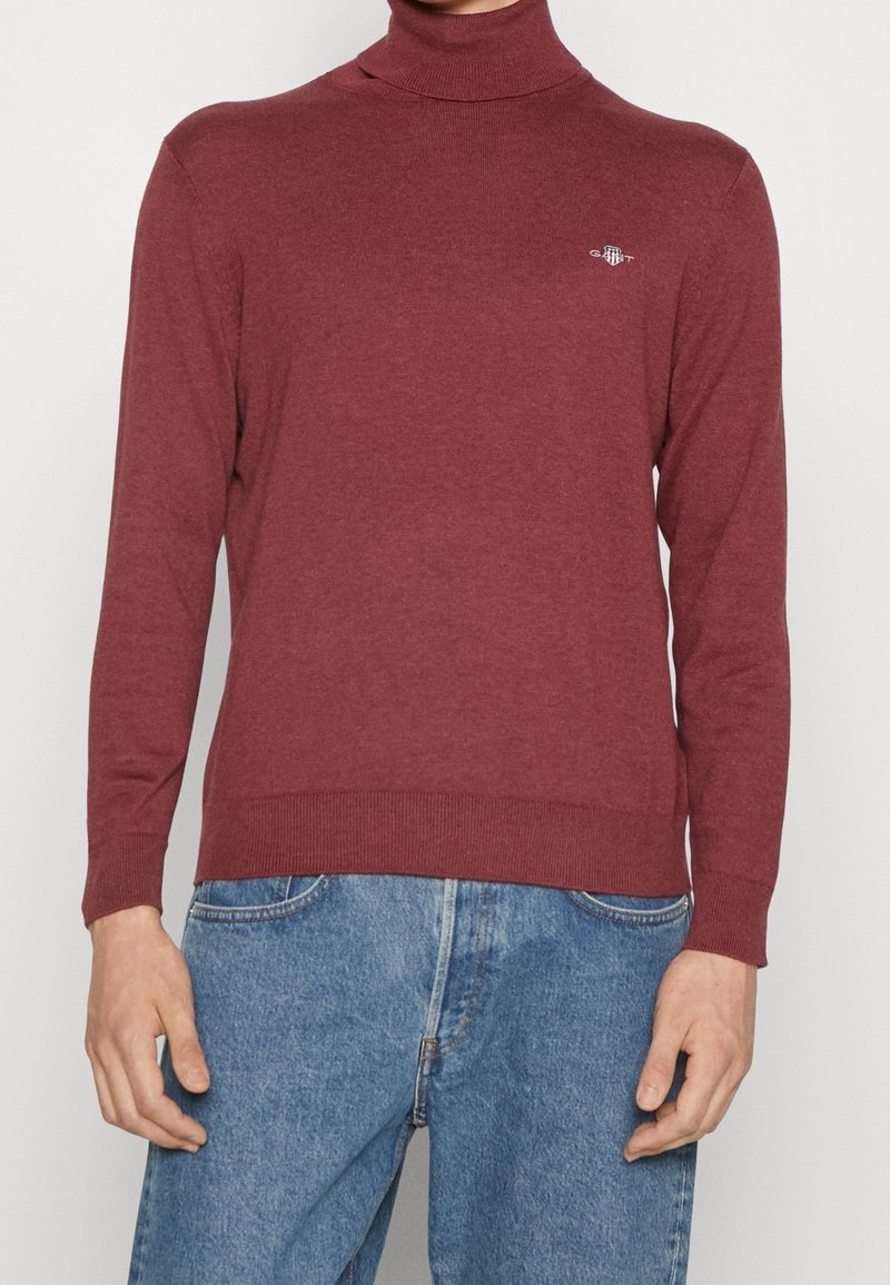 Bordeauxfarbener Rollkragenpullover aus weichem Strickmaterial. Verfügt über lange Ärmel, gerippte Bündchen und Saum sowie ein dezentes Logo auf der Brust.
