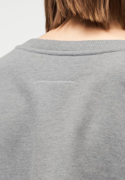Siv pulover z rebrastim izrezom in gladko teksturo. Prikazuje bližnji posnetek hrbtnega dela, kjer so poudarjene podrobnosti šivov in kakovost tkanine.