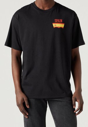 T-shirt en coton noir avec l'inscription rouge "SPAIN" et un accent avec le design du drapeau espagnol sur la poitrine. Manches courtes, col rond.