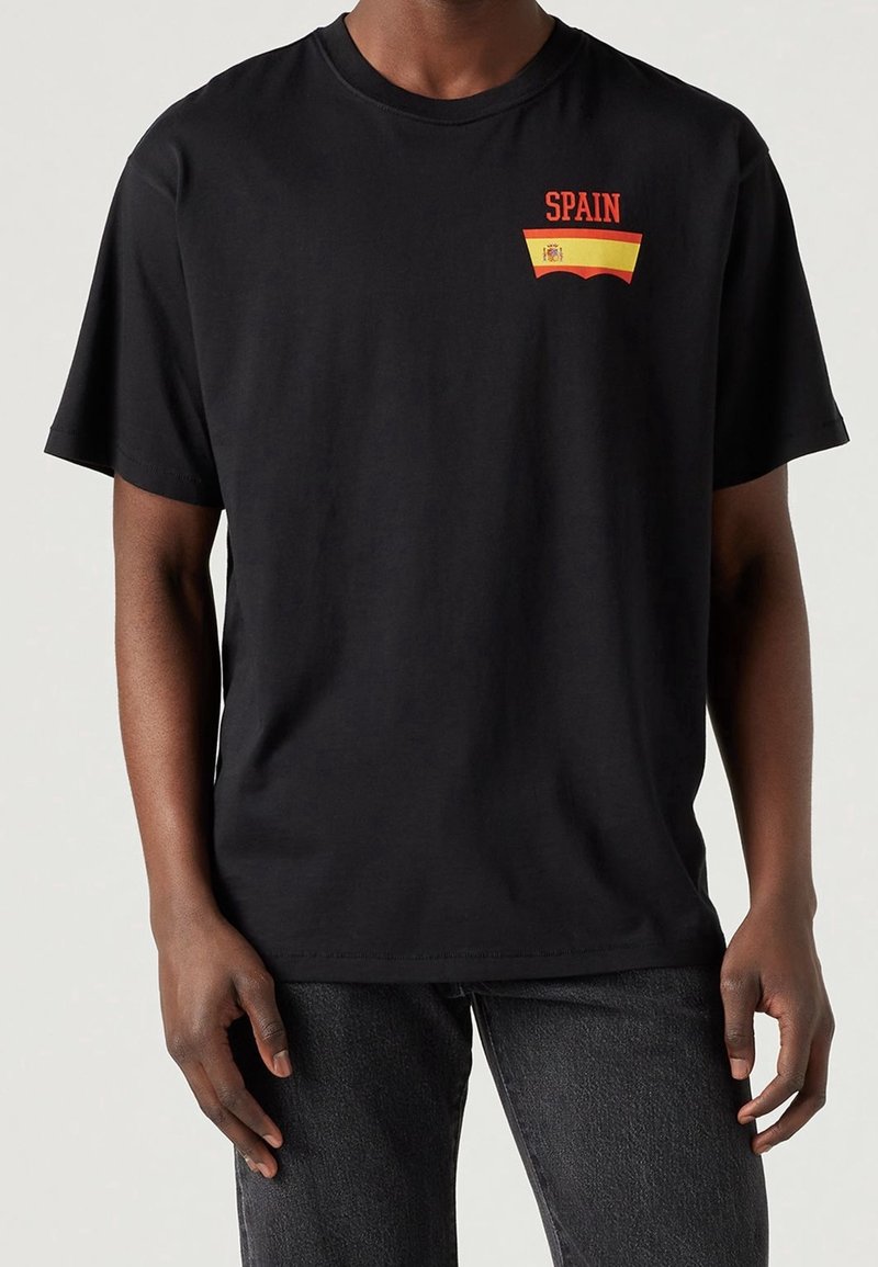T-shirt en coton noir avec l'inscription rouge "SPAIN" et un accent avec le design du drapeau espagnol sur la poitrine. Manches courtes, col rond.