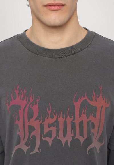 T-shirt gris avec un motif dans des tons de rouge ressemblant à des flammes, avec une lettrage en gras. Encolure classique et texture douce.