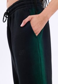Černé a zelené kalhoty s elastickým pasem, bočními kapsami a jemně vyšívaným logem na levé noze.